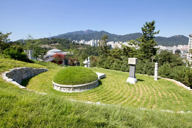 잔디 언덕 위 비석, 뒤로 보이는 기념관 지붕과 산