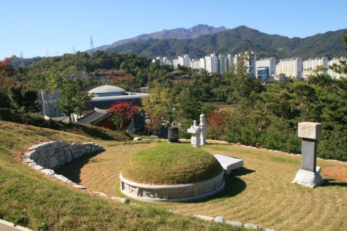 가을 잔디 언덕 위 비석, 뒤로 보이는 기념관 지붕과 산